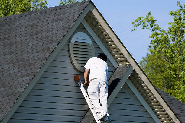 Painter working at the top of an extension ladder on a two story suburban home